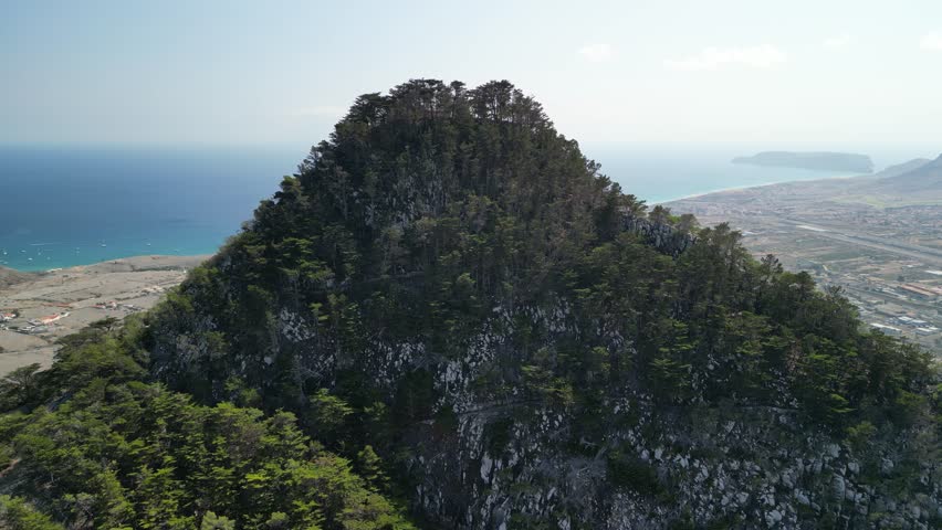 Aerial view of drone flying around Pico do Castelo mountain, with a shape of a vulcano. Porto Santo Island, Madeira, Portugal. Airport and long beach in the background