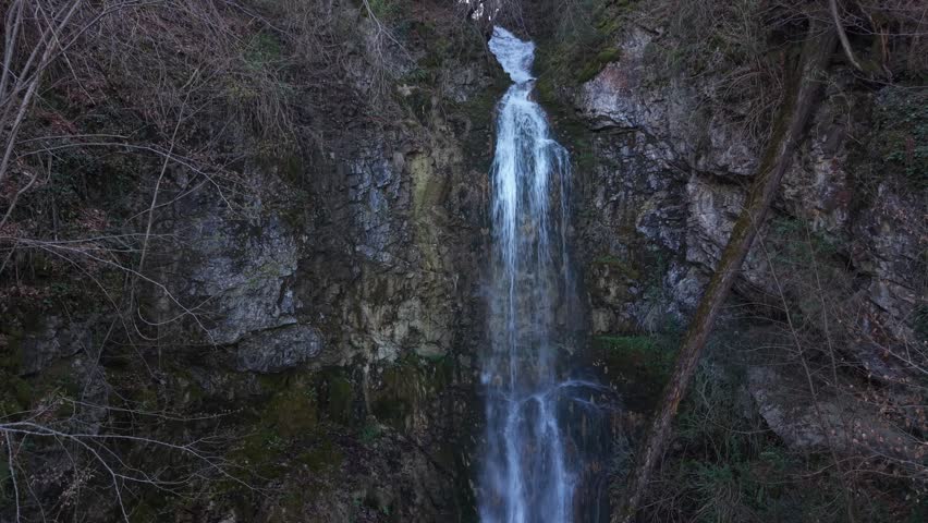 Static aerial view capturing a waterfall and the flowing river leading into it, surrounded by rocks and natural terrain.