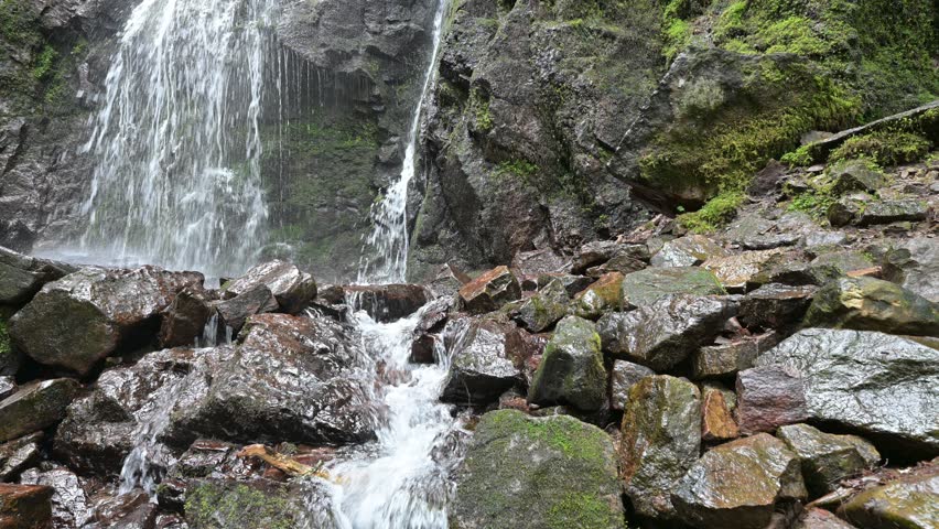 Peaceful waterfall flowing over rocks in a forest. Static nature scene with flowing water, wet stones, and lush greenery, creating a relaxing and meditative mood