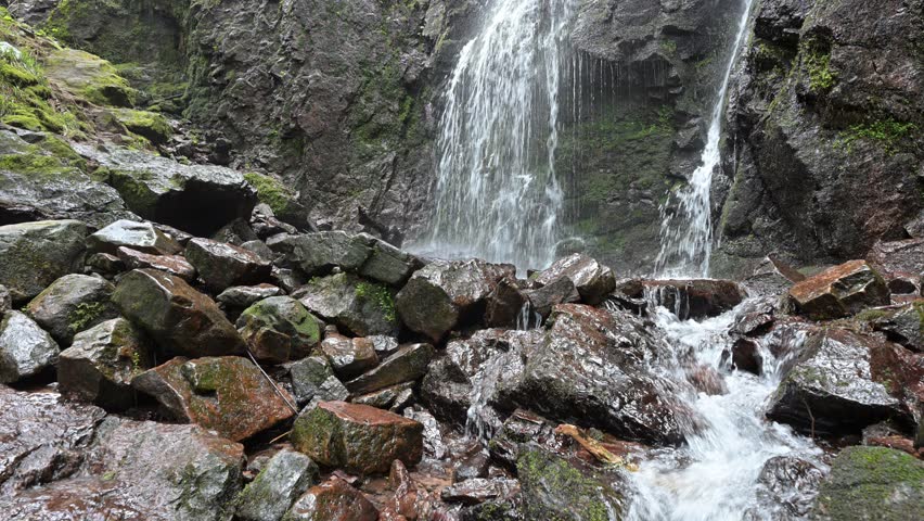 Peaceful waterfall flowing over rocks in a forest. Static nature scene with flowing water, wet stones, and lush greenery, creating a relaxing and meditative mood