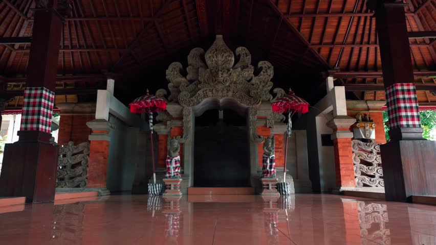 Symmetrical view of a beautiful traditional stone gate featuring red umbrellas, guardian statues, and pillars wrapped in checkered poleng cloth.