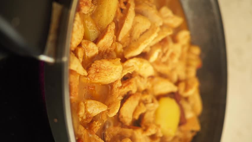 Chicken and potatoes cooking in a pan with sauce, generating steam and motion from the heat, delicious meal preparation.