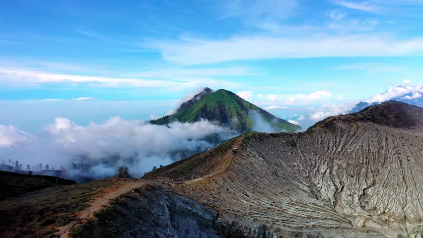 Aerial Panorama View of Volcano Crater Rim with Textured Grey Ash Slopes and Lush Green Mountain Peak Kawah Ijen. Horizon Rising Above White Clouds in East Java Indonesia. Wild Nature Landscape 4k