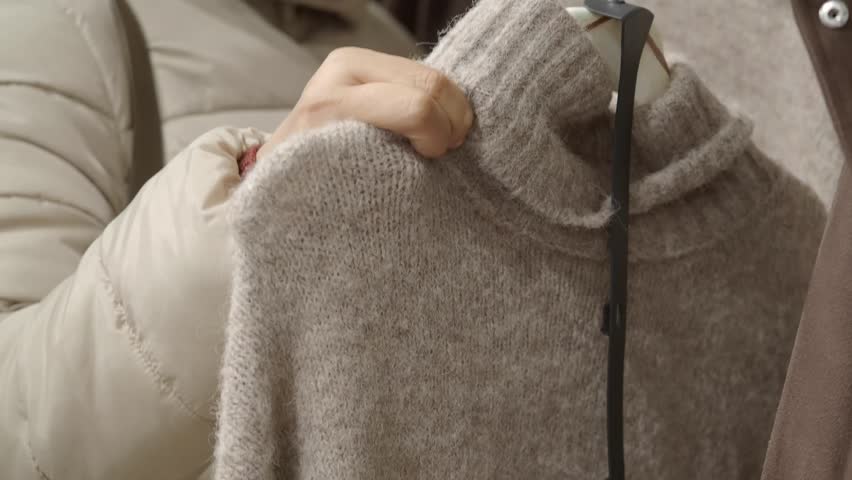 Female shopper choosing comfortable woolen garment in fashion boutique, close-up on woman hands holding knitted pullover.