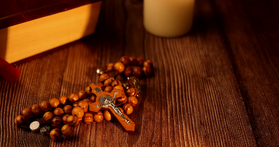 Traditional olive wood rosary with silver cross and white candles by a bible for representing christianity and religious worship.