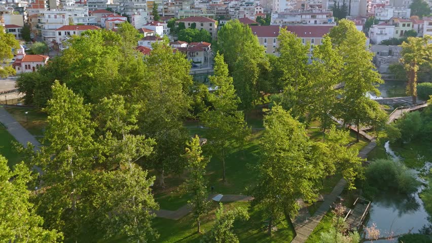 Aerial perspective of Agia Varvara Park in Drama, Greece. This natural urban oasis features crystal clear water springs, wooden bridges, traditional watermills, and lush green plane trees.