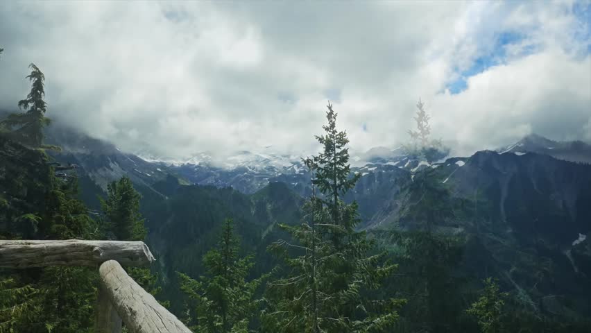 A scenic view from the Spray Park Trail in Mount Rainier National Park, Washington State. The footage captures a dramatic mountain landscape with dense evergreen forests in the midground, snow-capped