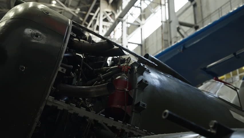 Close-up view of a propeller aircraft undergoing maintenance inside an industrial hangar, exposing engine components, landing gear, and fuselage details under workshop lighting