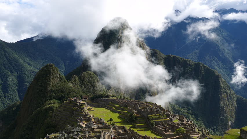 Machu Picchu Ruins with Clouds Flowing Over Huayna Picchu, Peru. Close-up view of the ancient Inca citadel of Machu Picchu with Huayna Picchu mountain in the background. Atmospheric clouds and mist drifting across the Andes create a dramatic scenic landscape. Iconic UNESCO World Heritage site in Peru. No people.