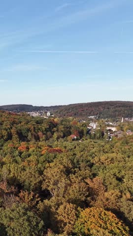 Autumn forest covering hills with a small town in the valley under blue sky