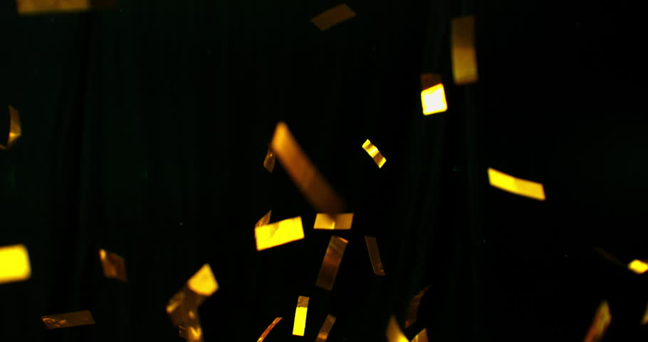 Golden confetti flying in super slow motion against a black background. Shiny metallic particles drifting and falling in the air, creating elegant festive atmosphere with dramatic lighting.