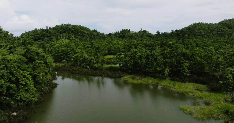 A scenic landscape of a lake surrounded by forest and green hills in Siargao, Philippines.