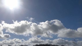 White cumulus clouds floating across a bright blue sky with the sun shining and flaring - Powered by Shutterstock - Get 15% off with code: PIKWIZARD15
