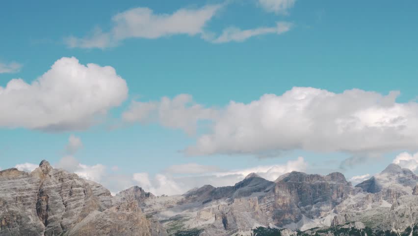 Wide-angle panorama of the Italian Dolomites. Dramatic limestone peaks under a blue sky with scattered clouds. Cinematic high-altitude landscape for nature and travel productions