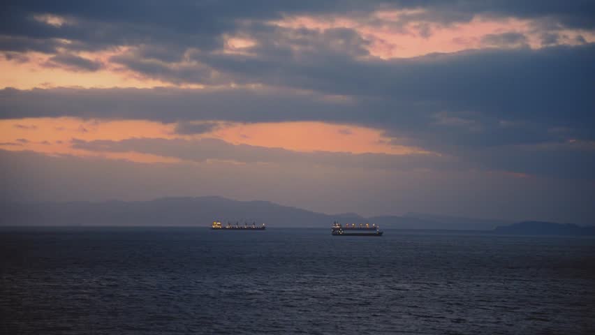 Ships sailing on dark ocean during dramatic sunset with clouds and distant mountains