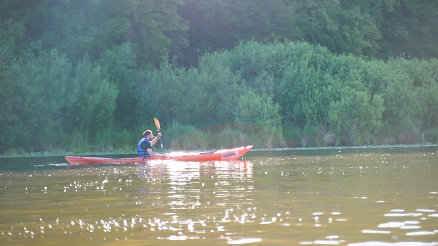 Kayaker paddling on calm lake at sunset