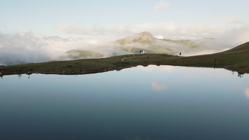 Tourists with a dog standing by the mirror-like Koruldi Lakes in Georgia. A peaceful mountain landscape in Svaneti with reflections, hiking, and pet-friendly adventure in Georgia Alps