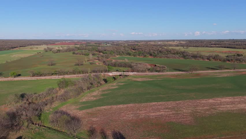 Aerial orbit over rural farmland with road and creek in early spring Oklahoma landscape