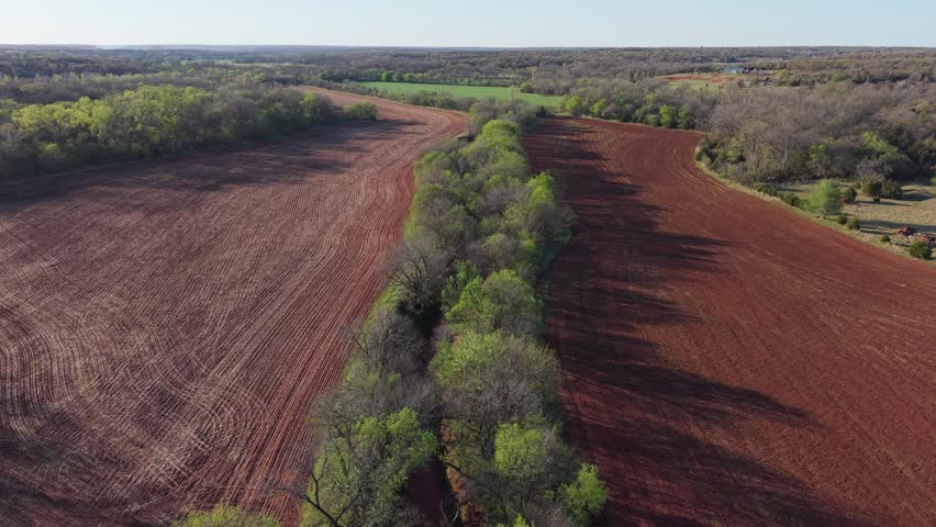 Aerial push forward over creek dividing farmland fields in early spring Oklahoma landscape