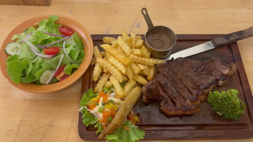 Juicy grilled picanha steak served with crispy fries, fresh salad, vegetables, and sauce on a wooden board