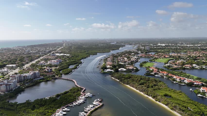 Aerial drone footage of the Intracoastal Waterway in Jupiter, Florida, USA, filmed on April 4, 2026. Boats navigate calm turquoise waters lined with luxury waterfront homes, marinas, and lush tropical vegetation. Cinematic overhead view capturing the coastal lifestyle and marine activity along one of South Florida’s most iconic waterways.
