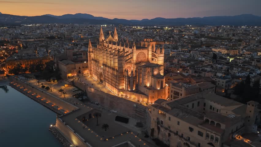 Evening view of the illuminated Cathedral of Santa Maria in Palma, Mallorca aerial footage of the city lights and harbor at dusk. Majestic Palma Cathedral in Mallorca glowing in the evening darkness