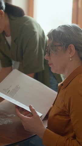 Vertical shot of multigenerational family making dough with recipe from book in cozy home kitchen