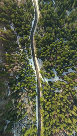 Winding mountain road aerial top down view through snowy forest