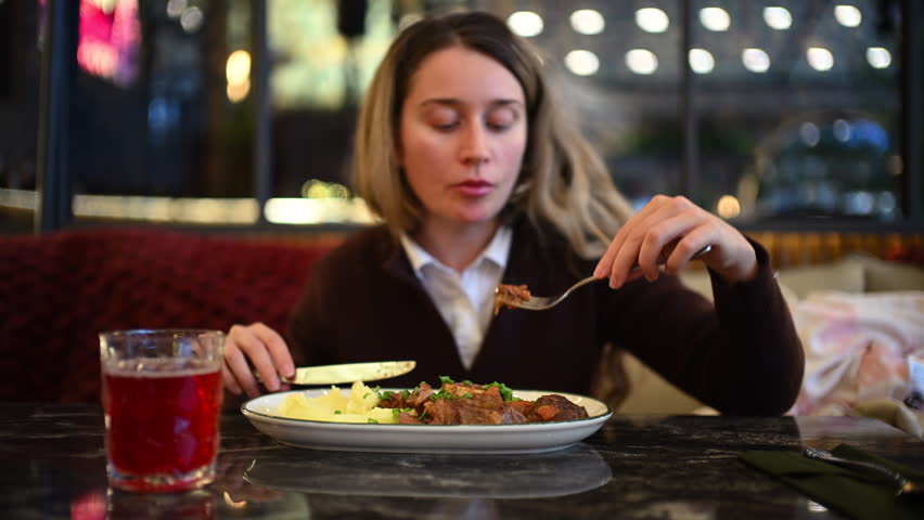Woman eating mashed potatoes and meat at a restaurant table using fork and knife