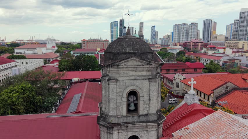 Close aerial drone view of San Agustin Church bell tower in Intramuros, Manila, with modern skyline in the background. Historic UNESCO landmark and colonial architecture.