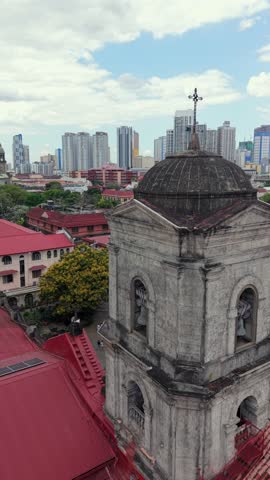 Close aerial drone view of San Agustin Church bell tower in Intramuros, Manila, with modern skyline in the background. Historic UNESCO landmark and colonial architecture.