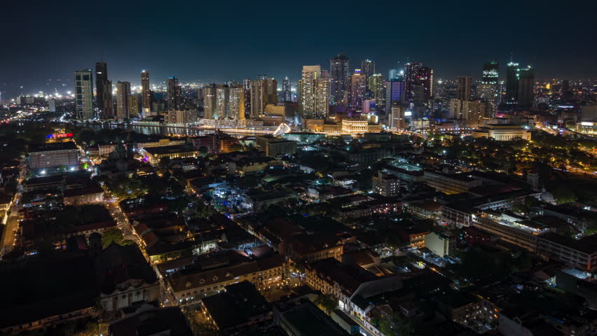 Aerial night timelapse of Manila skyline in the Philippines, featuring illuminated skyscrapers, glowing city lights, and modern urban architecture in a vibrant Southeast Asian metropolis.