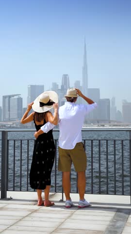 A beautiful tourist couple on a sightseeing trip enjoys the view of the skyline of Dubai, UAE, as a city travel concept