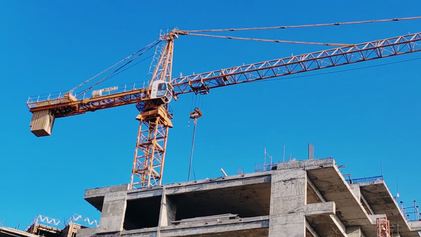 Modern high-rise residential building under construction, comprising reinforced concrete structural framework. Equipped fixed yellow tower crane and external scaffolding surrounding multi-level façade