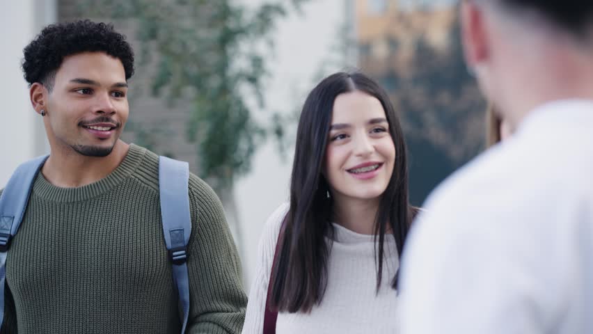 Happy university students enjoying a conversation outside after class. Young diverse group of friends smiling and talking on campus