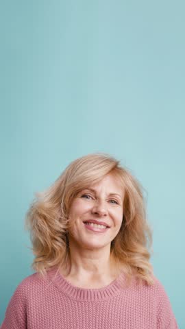 Headshot of a happy mature woman with blonde hair smiling and looking at the camera. Beautiful senior lady posing in a studio with a blue background