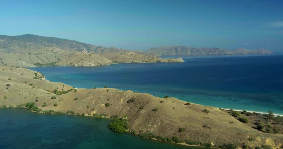 Drone aerial view of green island hills and coastline surrounded by ocean. The natural landscape creates a calm and scenic tropical environment.