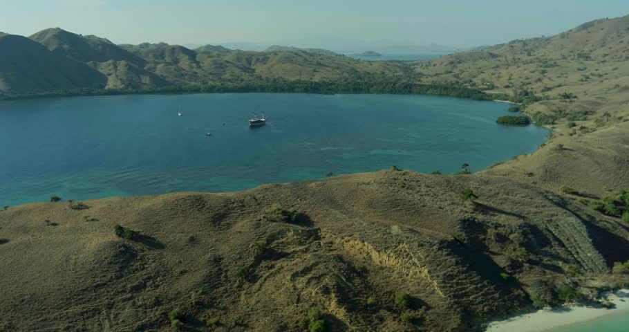 Aerial drone shot of tropical island hills and coastline surrounded by ocean. The natural scenery creates a calm and cinematic tropical environment.