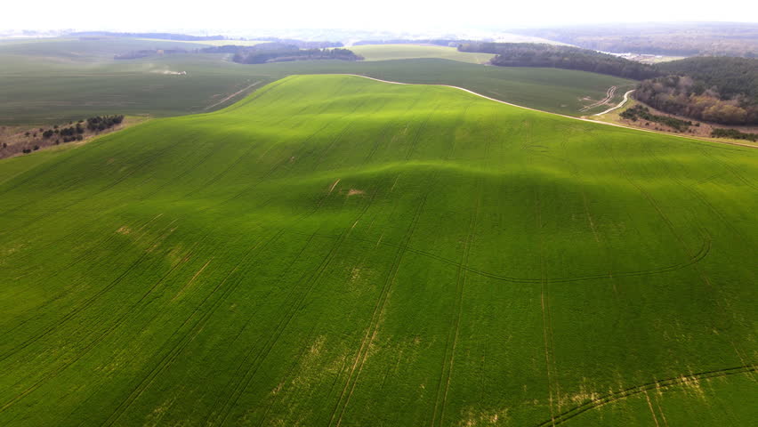 Aerial view of green rolling hills and agricultural farmland with cloud shadows moving across the landscape in springtime