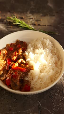A warm bowl holds fragrant chicken curry with colorful peppers beside a serving of fluffy white rice.