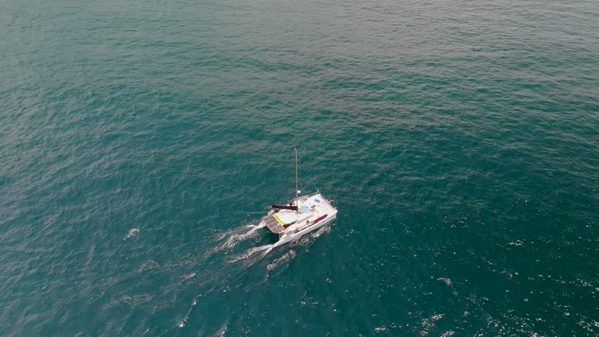 A white yacht sails in the blue ocean among endless waters, aerial view