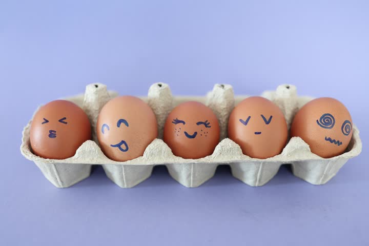 Eggs with funny faces in box. Happy, angry, sad, surprised faces on brown eggs. Stop motion. Funny cartoon faces. Food concept. Close-up of hen eggs. 