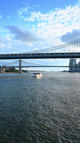 Travelling on board of the boat with American flag at front by the East River. The Manhattan Bridge and the Brooklyn Bridge. Vertical video.