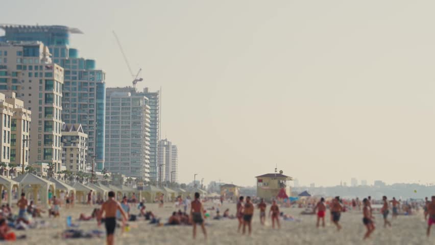 People enjoy playing at the beach in Tel Aviv Israel on hot sunny summer day. Locals and tourists swimming in sea and sunbathing on sand while others play with ball during vacation or weekend