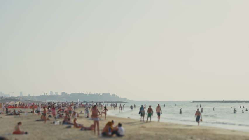 Local people and tourists enjoy Tel Aviv beach and Mediterranean Sea in summer. Old city of Jaffa or Yafo in background. People play swim and sunbathe on the sand by fresh water in Israel