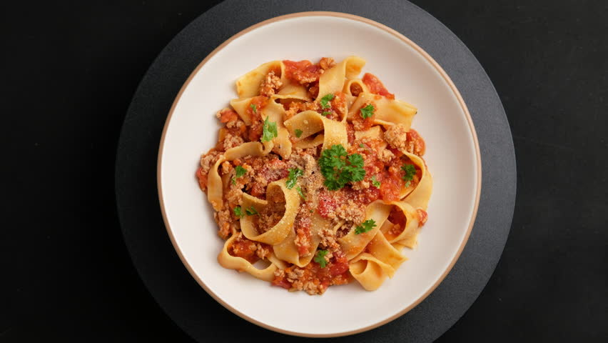 pappardelle pasta with Ground meat and tomato,spaghetti with a meat based bolognese tomatoes,served on white plate with parmesan cheese.Top view.