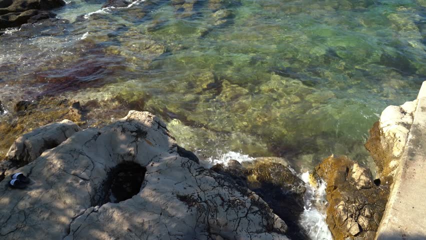 Gentle waves of the sea brushing over the rocks on the shore in Croatia. A pair of flippers are laying on the side.