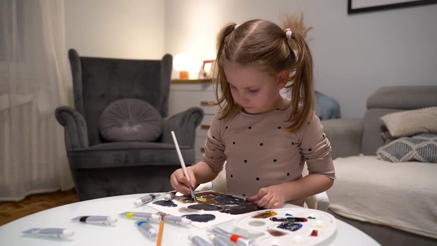 Cute little girl painting at home in her room with tempera paints 