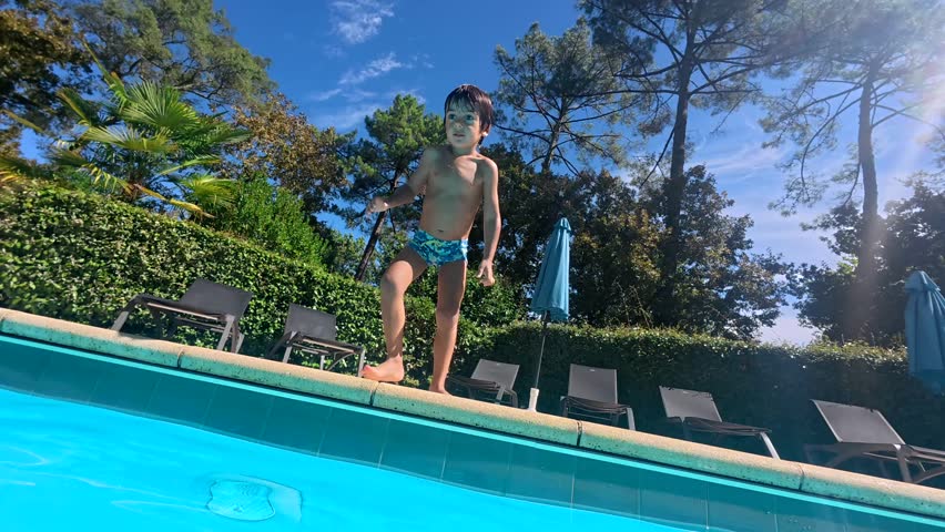 Happy boy jumping into the bright blue swimming pool on a sunny summer day, filmed from the joyful perspective of his father who catches him in the water for a fun family moment