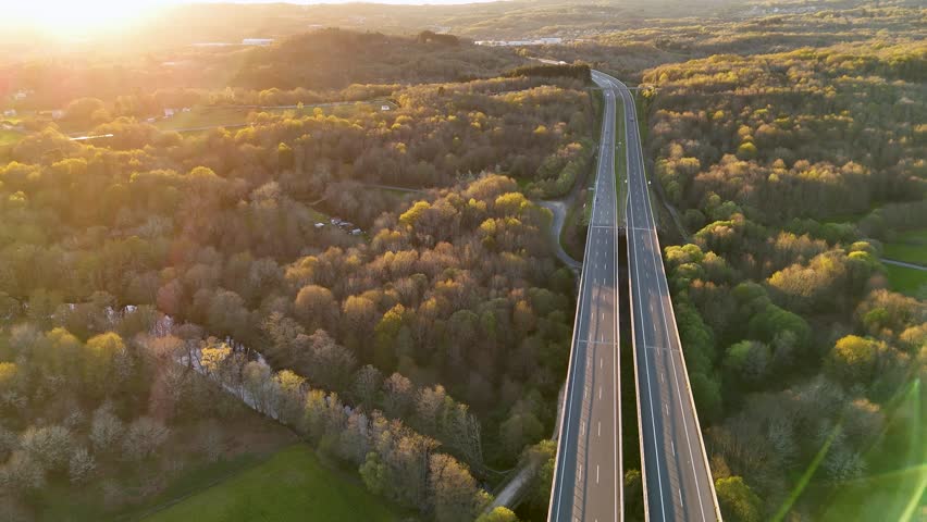 Aerial view of a highway passing through a lush forest landscape during a beautiful sunset